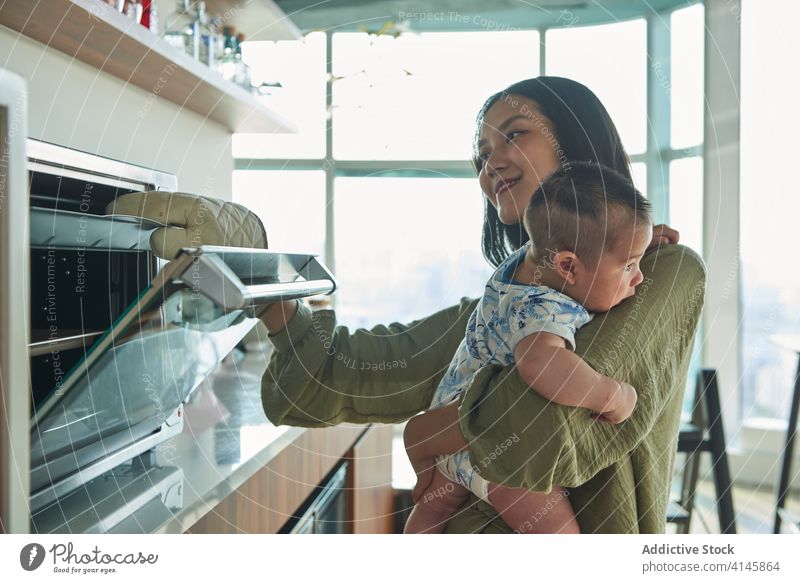 Mother cooking in the oven holding her baby family child soon boy dad father dady mom mother fun enjoy home at home stay at home beautiful model portrait