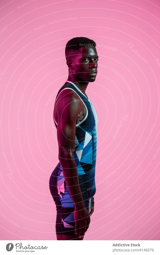 Black athlete exercising in neon lights sportsman exercise stand training energy strong serious perform practice brutal looking at camera determine active