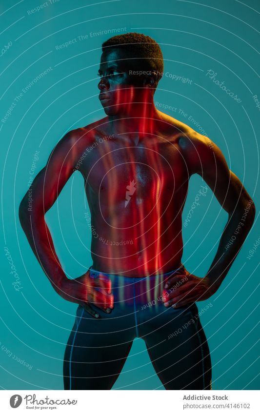 Shirtless athlete standing in colorful studio sportsman runner shirtless muscular determine confident active physical neon young black african american ethnic