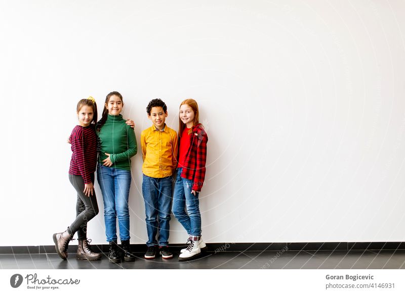 Portrait of cute little kids in jeans  looking at camera and smiling, standing against white wall caucasian boy school girl female childhood children casual