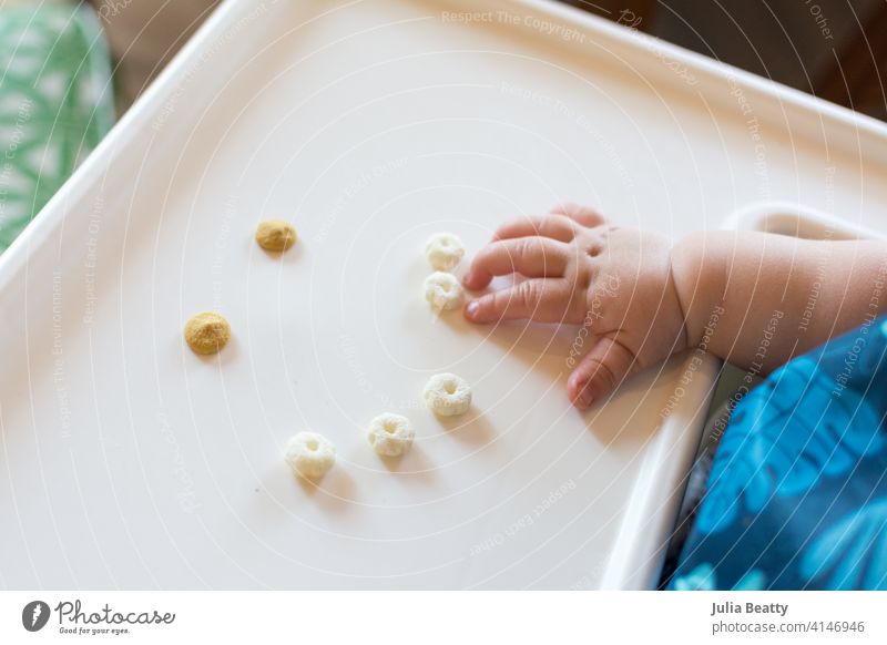 Smiley face made of cereal puffs and yogurt drops on a high chair tray; baby reaching out to self feed infant child 6-12 months old finger food smile