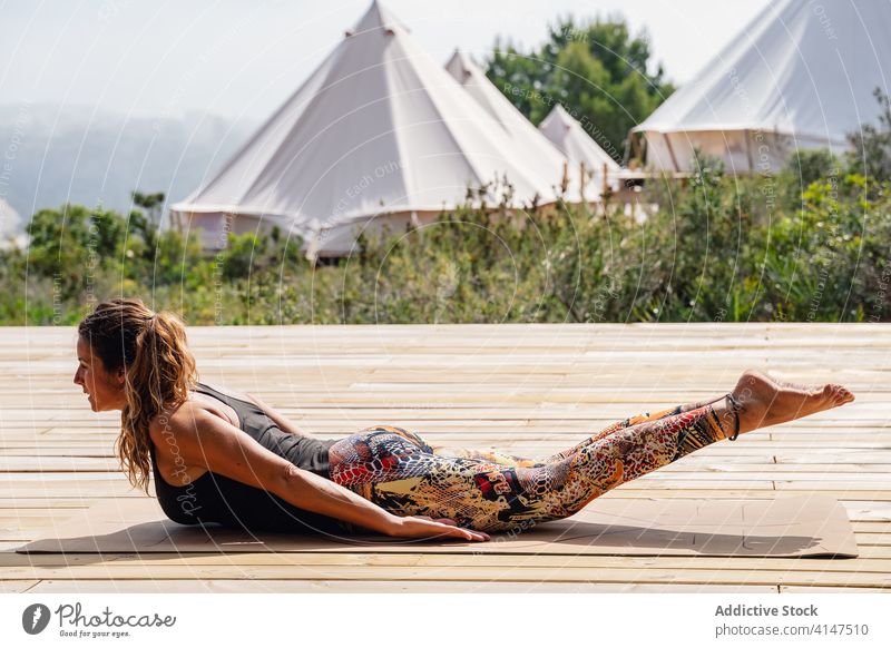 Concentrated woman doing Locust asana during outdoor yoga session locust salabhasana camp stress relief stretch balance wellness practice wooden platform