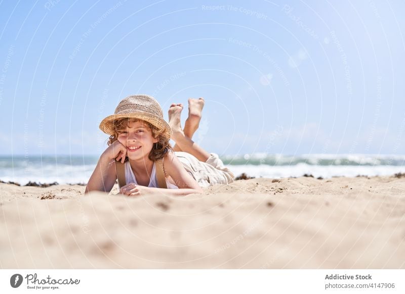 Smiling boy on sandy coat during summer holidays cute lying prop chin rest seashore beach barefoot resort carefree seaside vacation little coast kid child happy