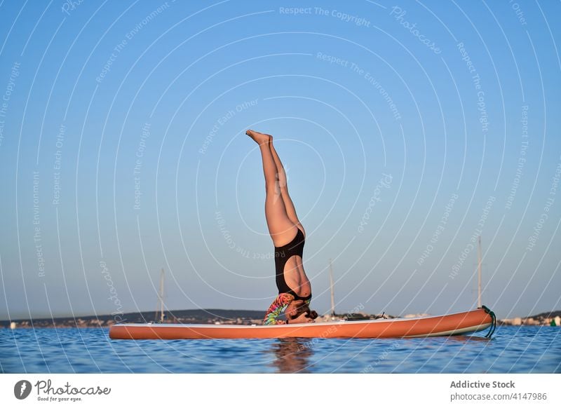 Unrecognizable woman doing yoga in Supported Headstand position surfer paddleboard headstand asana salamba sirsasana sea water amazing female sunset twilight