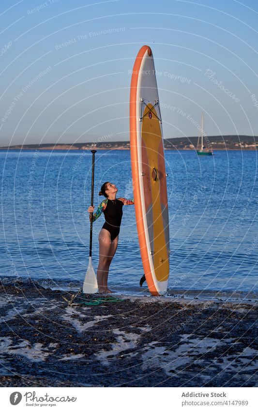 Woman with paddleboard on shore in sea surfer pump woman beach equipment water seashore female sport relax ocean coast activity stand holiday sun lady tool