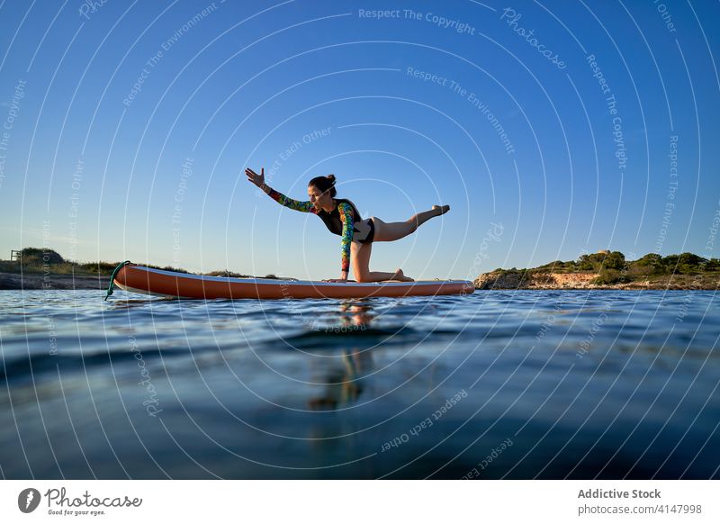 Calm woman doing yoga in Balancing Table pose balance balancing table pose sea paddleboard surfer concentrate calm female sunset water practice nature harmony