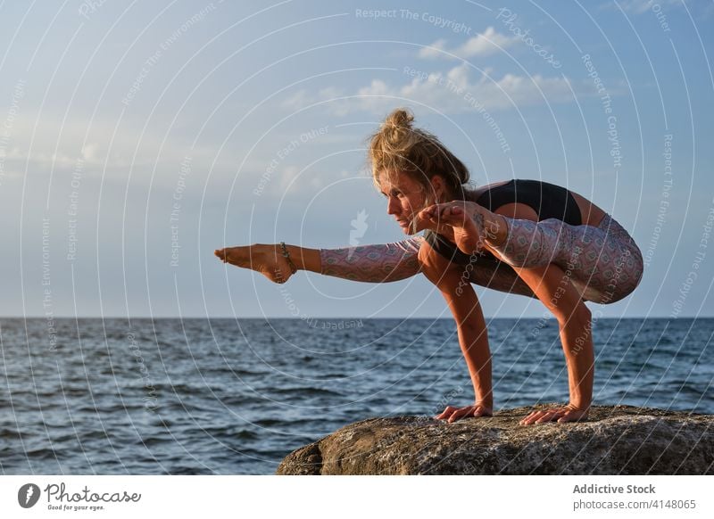 Woman in a rock facing the sea doing a variation of handstand yoga pose concentration strength copyspace raise beach isolated fitness sport health woman girl