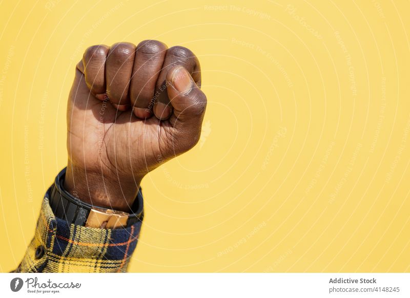 raised fist of a black man on a yellow background protest person right fight power hand freedom strength human revolution strong arm up anger punch rebellion