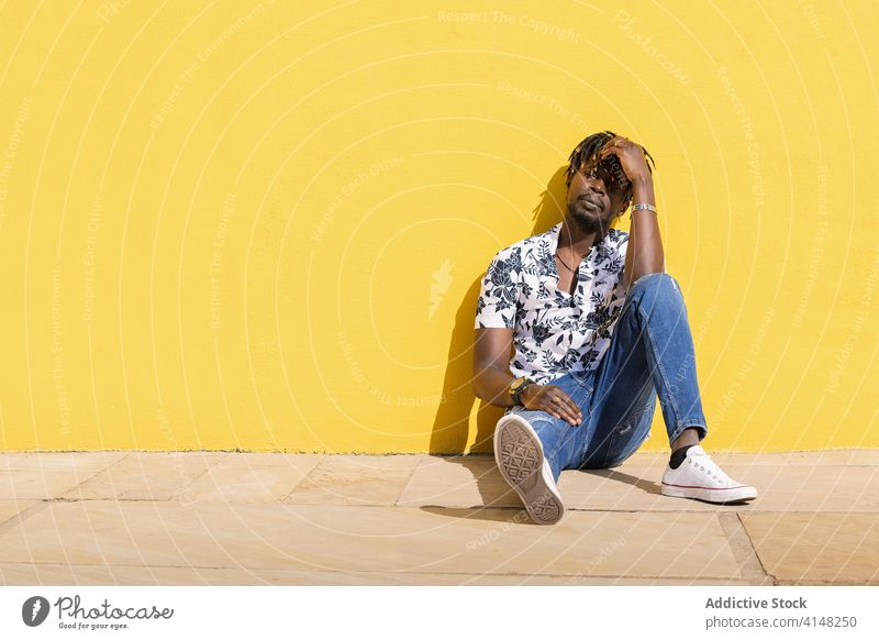 black man sitting on the floor against yellow wall person leaning lifestyles looking pensive guy relaxation copy space confidence cool horizontal alone handsome