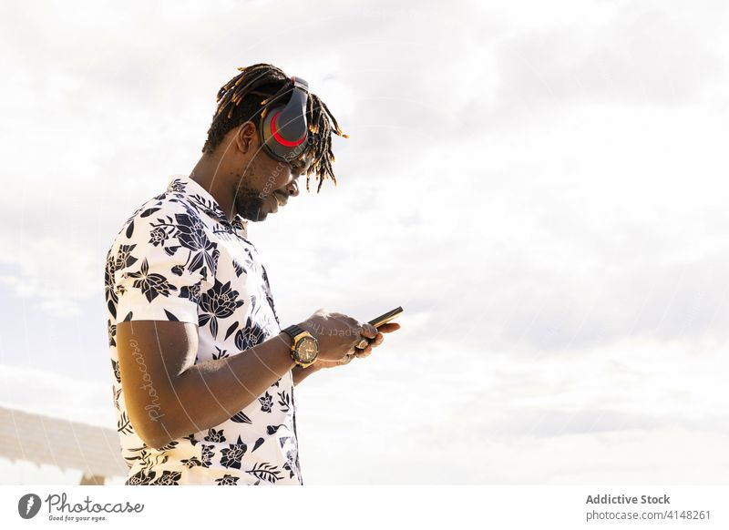 young black man with headphones looking at phone person african male music american technology mobile listening communication mobile phone portrait happy modern