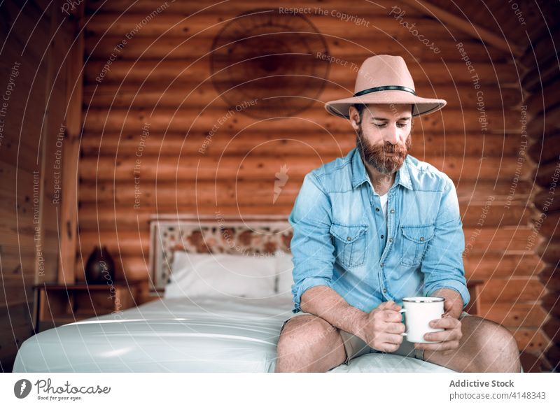 Bearded man on bed in wooden house fresh morning coffee traveler rustic comfort male rest sit cozy home enjoy relax drink beverage breakfast chill cup guy beard