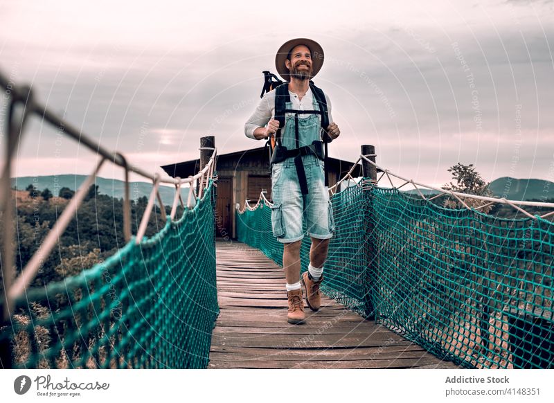 Traveling man walking along wooden footbridge suspension tourist backpack admire landscape vacation male adventure trip tourism content journey traveler young