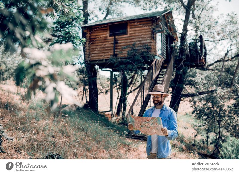 Cheerful traveling man orientating on map in forest find location orientate traveler paper navigate tourist hut male tree house tourism guide explore journey