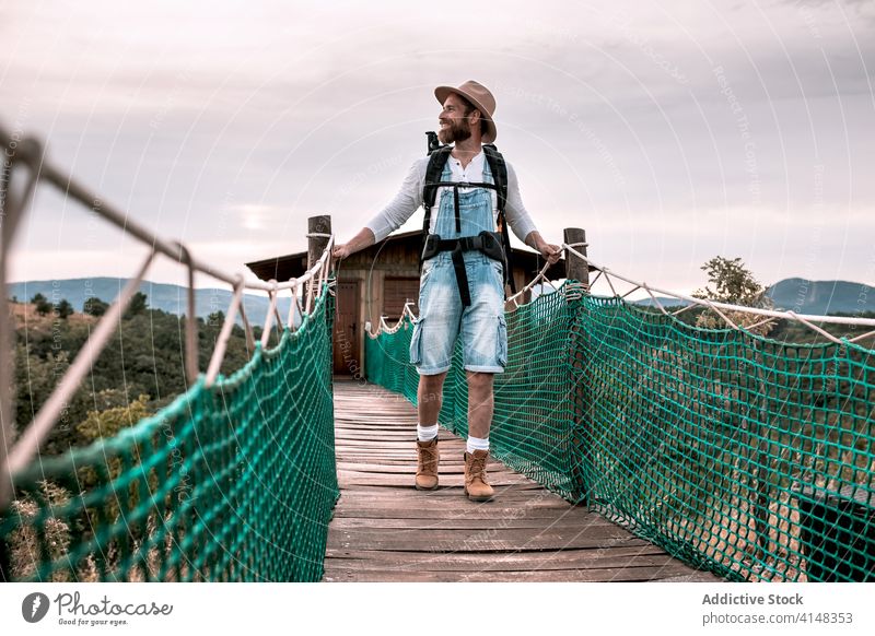 Traveling man walking along wooden footbridge suspension tourist backpack admire landscape vacation male adventure trip tourism content journey traveler young