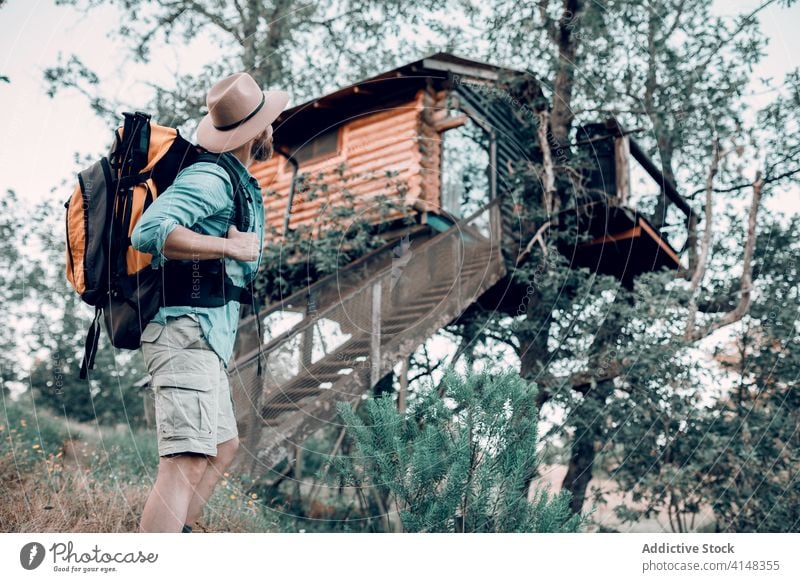 Traveling man near tree house in woods forest traveler backpack wooden building adventure male stand tourism journey nature holiday landscape green trip