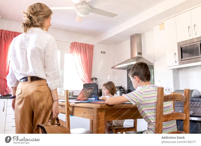 Children doing homework using laptop near stylish mother in kitchen children education knowledge study learn gadget device tablet netbook modern style
