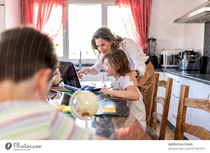 Mother with boy watching laptop near unrecognizable sibling in kitchen mother homework education interact share childcare son show using gadget device netbook