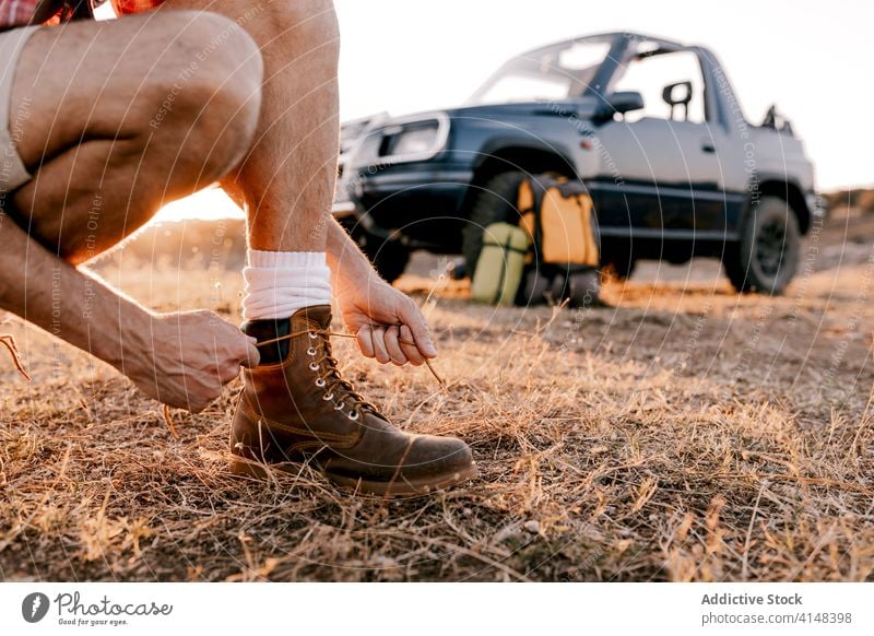 Faceless male traveler tying shoelaces on boots on faded grass tourist tie vacation harmony automobile backpack sunlight landscape nature car trip beauty sock