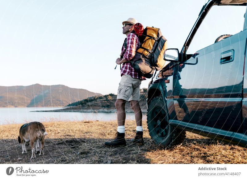 Tourist with backpack standing near dog and car admiring nature tourist contemplate highland travel automobile river mountain idyllic harmony picturesque