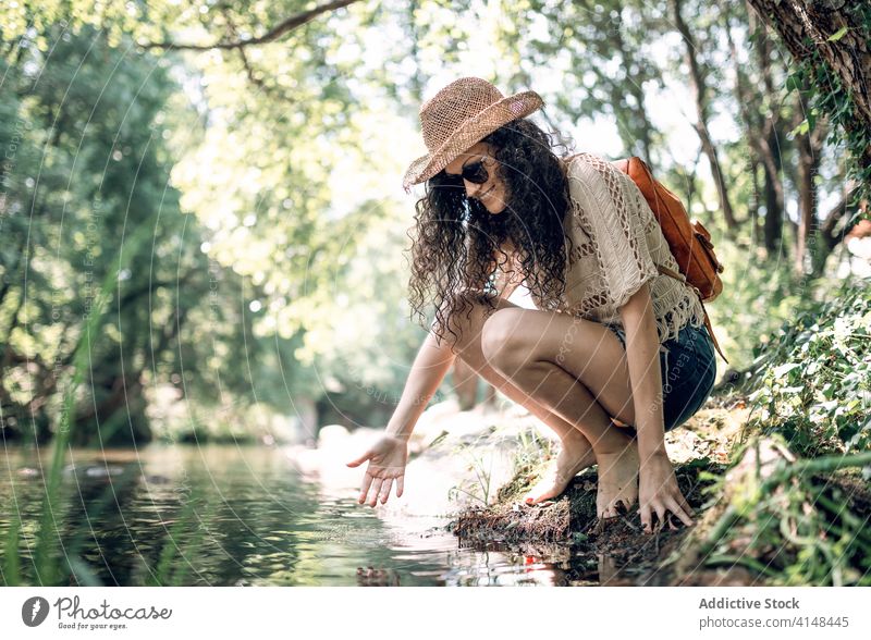 Traveling woman near river in forest travel tourist hat summer vacation sunglasses water holiday serene calm female nature stone shore weekend harmony tranquil