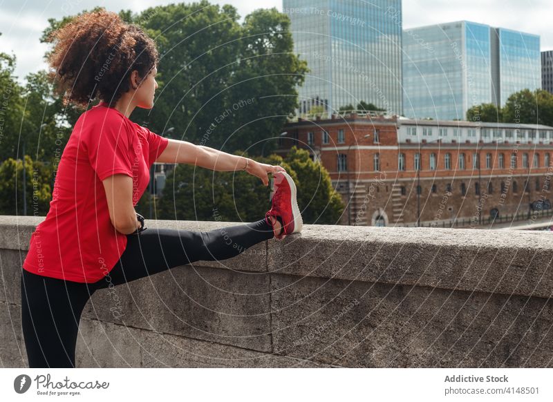 Unrecognizable ethnic athlete stretching leg during training on city bridge workout exercise sport flexible wellbeing warm up sportswoman sportswear urban