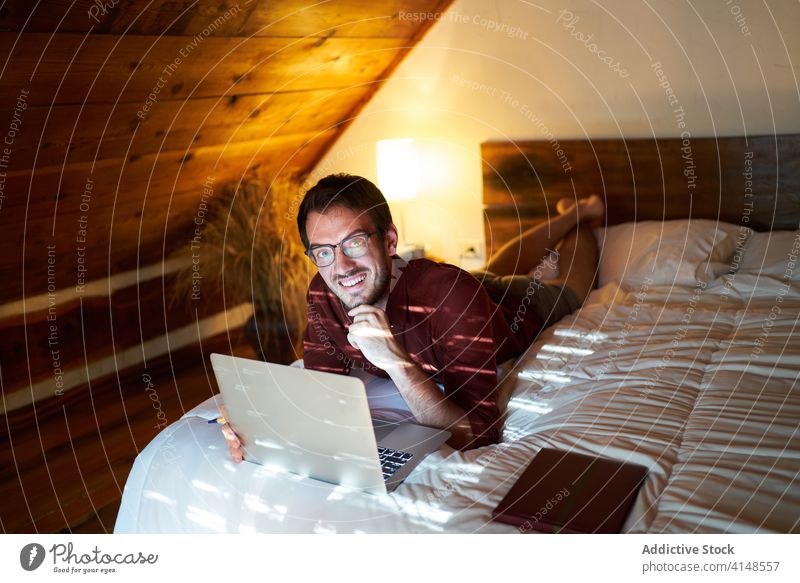 Concentrated male freelancer typing on laptop at home remote man work project entrepreneur using bed lying thoughtful browsing netbook internet device gadget