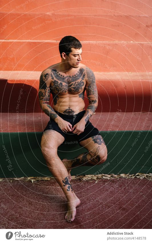 Brutal male athlete resting on steps on sports ground sportsman workout summer relax brutal shirtless serious healthy training sportswear confident tired fit
