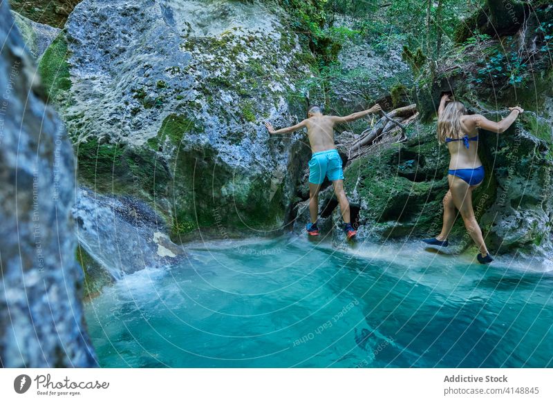 Traveling couple crossing river in summer climb cliff rock travel adventure rocky forest slope swimwear holiday activity freedom nature vacation together