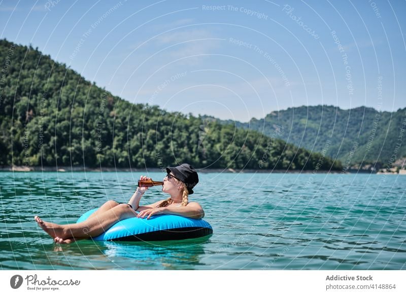 Carefree woman in inflatable ring on lake float summer relax mountain vacation beer female surface calm water sunny holiday joy weekend enjoy drink rest bottle