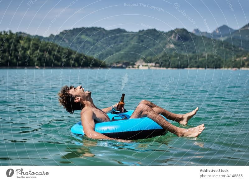 Carefree man in inflatable ring on lake float summer relax mountain vacation beer male surface calm water sunny holiday joy weekend enjoy drink rest bottle