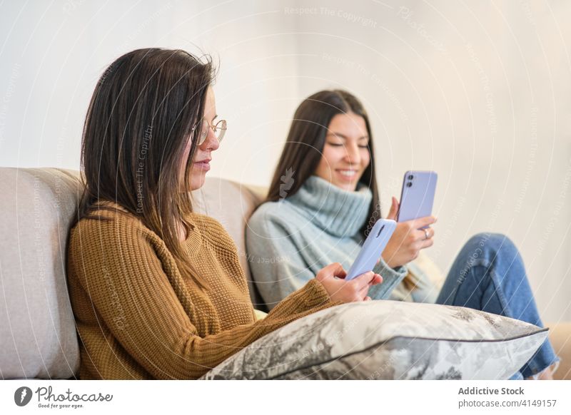 Happy women browsing cellphone together friendship social media smartphone best friend home using relax mobile weekend sofa rest device connection young chill