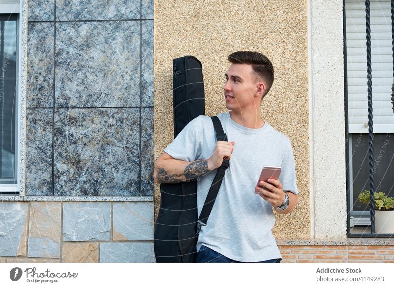 Man with guitar using smartphone in city read message social media man guitarist musician male content device gadget internet case urban building cellphone
