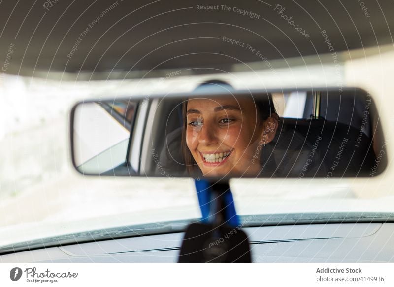 Smiling woman sitting in car driver mirror rearview transport vehicle automobile cheerful female modern trip reflection window positive road young happy smile