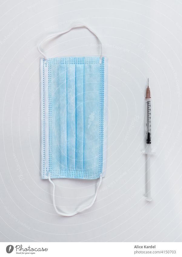 Protective mask and a vaccination syringe with the needle on white table. Vaccine ready. Danger or salvation? Coronavirus Vactination. Syringe Mask Virus