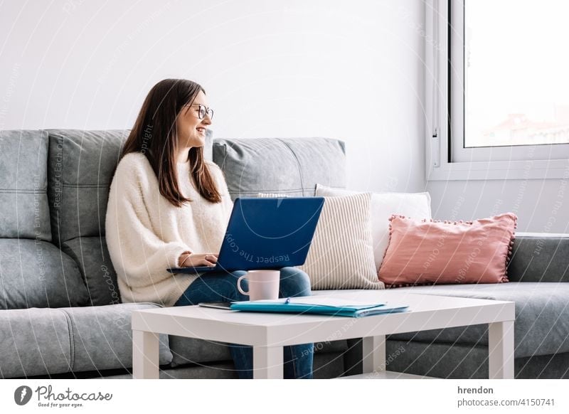 woman with laptop on her sofa at home indoor using working office conversation job notebook young happy typing study one woman only entrepreneur freelancer