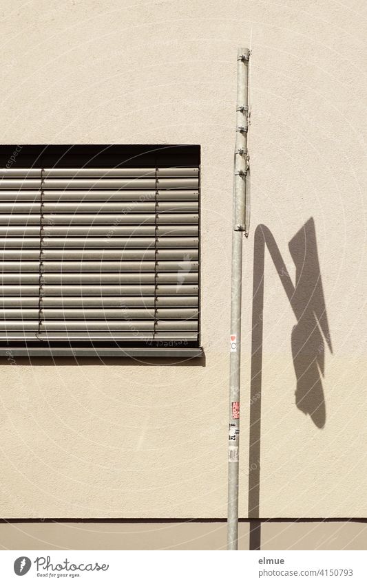 a grey blind covers the window next to a traffic sign with shadows cast on the beige facade / living Window blinds Window roller blind dwell Road sign Shadow