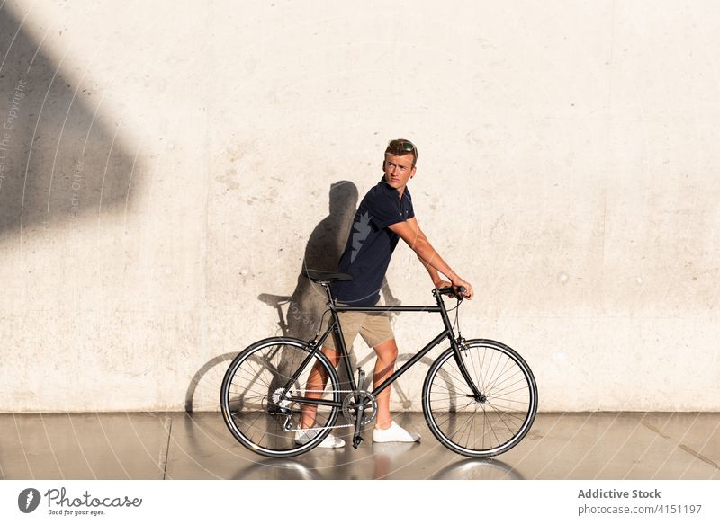 Man with bicycle on concrete wall adult bike blond casual caucasian copy space cycling cyclist lifestyle male man millennial mobility modern people serious