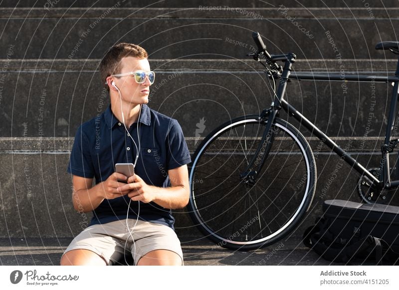 Man sitting on stairs on the smartphone bicycle bike blond business caucasian mobile phone communication copy space cycling cyclist entrepreneur freelance