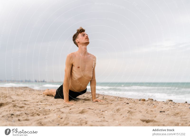 Yogi man in cobra pose on beach yoga practice Bhujangasana sand twist male yogi slim shirtless sea healthy lifestyle balance naked torso coast shore ocean
