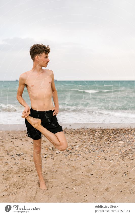 Flexible young yogi man standing on beach yoga practice sand half lotus pose ardha padmasana balance male flexible slim shirtless position concentrate posture
