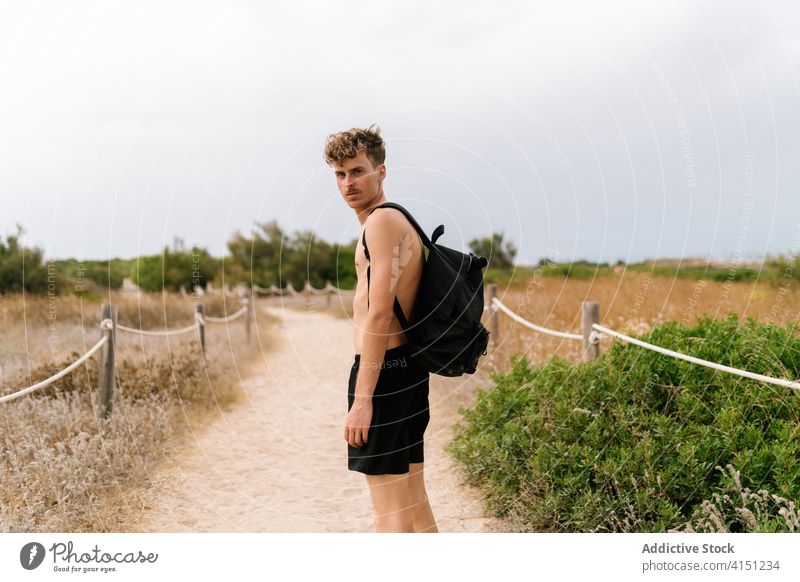 Young man with backpack standing on rural pathway active shirtless countryside young serious field male naked torso nature summer lifestyle freedom activity