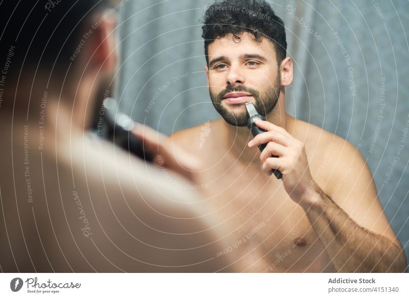 Brutal man shaving beard with trimmer at home grooming shave brutal bathroom serious handsome male concentrate focus confident determine masculine electric