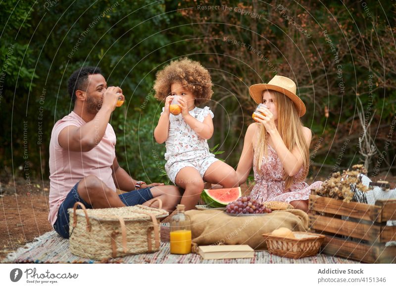 Young parents with kid drinking juice during picnic family healthy orange summer love relationship mixed race together enjoy fresh natural beverage fruit