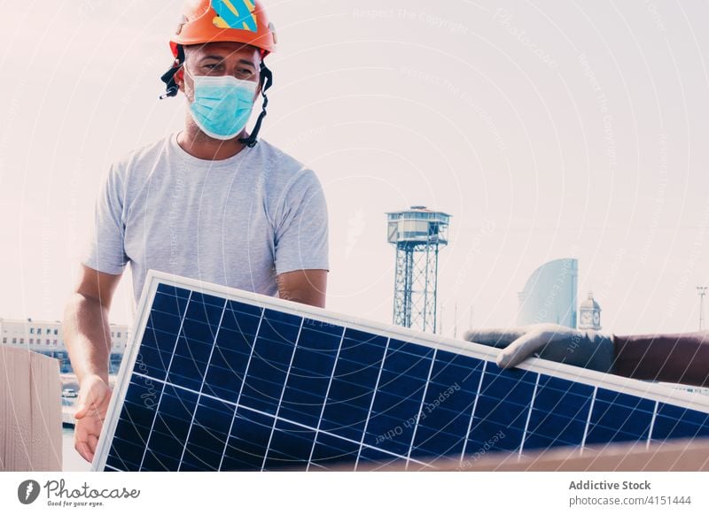 Male worker in mask with solar panel install battery man engineer alternative sustainable power male development energy resource industrial area plant daytime