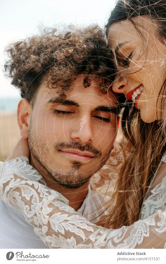Happy newlywed couple hugging on beach romantic happy cuddle gentle enjoy together relationship love embrace marriage eyes closed tender cheerful sensual smile
