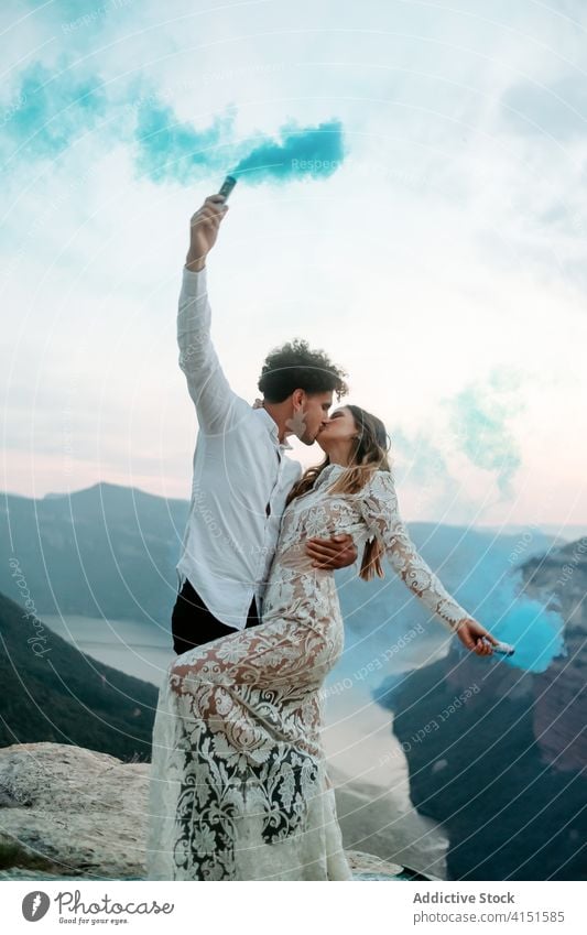 Newlywed couple with smoke bombs in mountains newlywed love celebrate rock romantic young happy kiss hug embrace cliff edge nature together relationship wedding