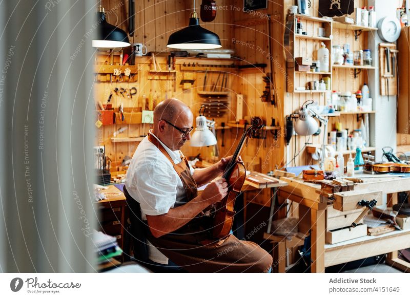 Craftsman with violin in professional workshop craftsman repair luthier artisan restore master skill male mature middle age maker handmade occupation workplace