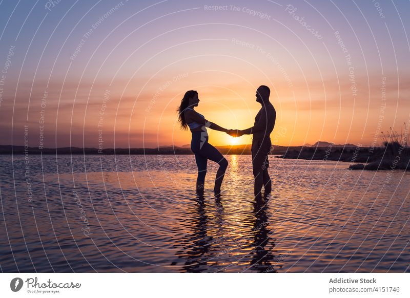 Unrecognizable couple standing at lake during sunset water active relationship holding hands romantic love silhouette nature twilight dusk summer lifestyle