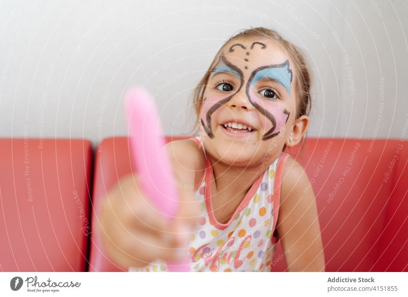 Happy child with painted face at home girl weekend having fun adorable picture pigment butterfly body art sofa cheerful relax sit kid joy smile comfort happy