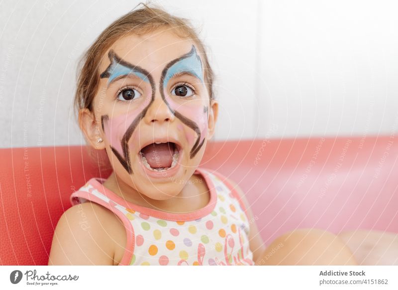 Happy child with painted face at home girl weekend having fun adorable picture pigment butterfly body art sofa cheerful relax sit kid joy smile comfort happy